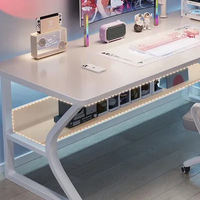 A white computer desk with various accessories, including a gaming keyboard, speakers, and decorative items, illuminated by LED strip lights.