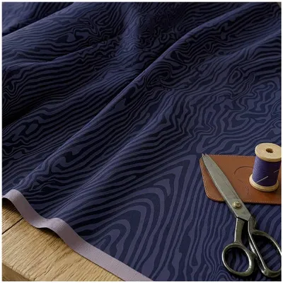 Nahaufnahme von French Terry Kombistoff What the Duck von Thorsten Berger in Lila, dekorativ drapiert auf einem Holztisch mit Garnrolle und Schere.