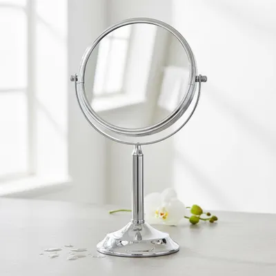 A silver vanity mirror is placed on a countertop next to a white orchid.