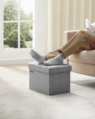 A person's legs are propped up on a gray ottoman in a bright room with large windows.