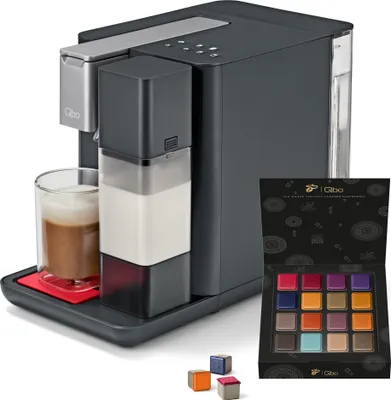 A coffee machine with a glass of coffee, a milk carafe, and a box of coffee capsules.