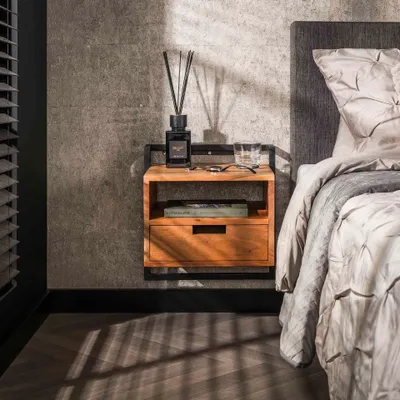 A bedside table with a drawer and an open shelf, next to a bed in a bedroom.