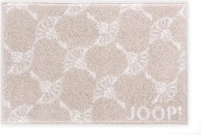 A beige bath mat with a white allover pattern and the JOOP! logo.