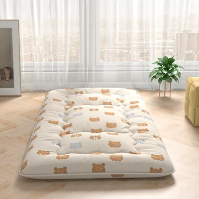 A floor mattress with a bear pattern, placed on a wooden floor in front of sheer curtains.