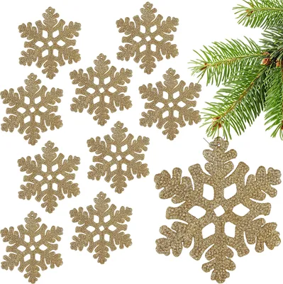 A collection of gold glitter snowflake ornaments arranged on a white background, with a sprig of pine tree branches in the upper right corner.