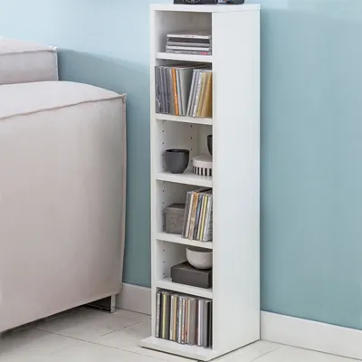 A white CD shelf unit stands next to a light-colored sofa against a light blue wall.