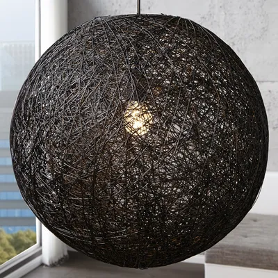 A large, spherical black pendant lamp made of interwoven threads hangs in a room with a window and a glimpse of a city skyline in the background.