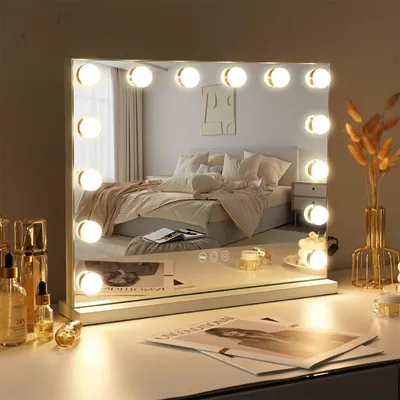A vanity mirror with lights is placed on a desk in front of a bed.