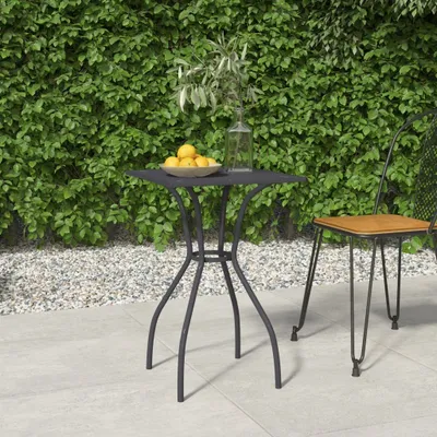 A small square table with a bowl of lemons and a vase of greenery on it, next to a chair on a patio.