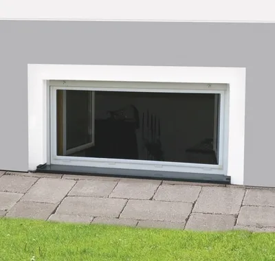 A white framed window installed in a gray wall, with a paved walkway and grass in front.