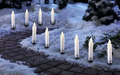 Candle-shaped lights are placed along a snowy path in a garden at night.