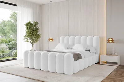 A modern white upholstered bed with a headboard and footboard, set in a bright, minimalist bedroom with large windows and natural light.
