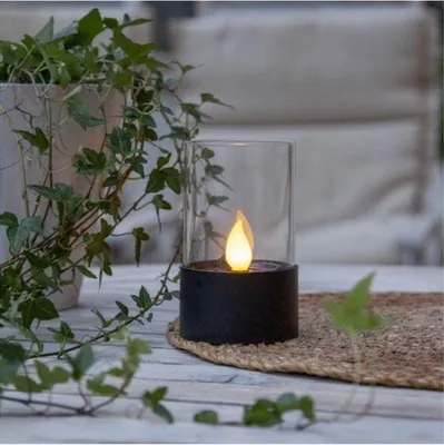 A solar-powered LED candle lantern sits on a table next to a potted plant.
