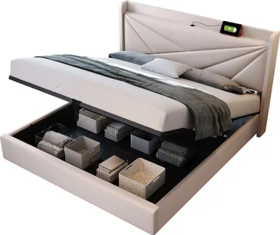 A beige upholstered storage bed with the mattress lifted to reveal storage bins underneath. A phone is charging on the headboard.