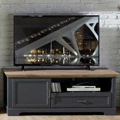 A TV stand with a television on top, placed against a brick wall.