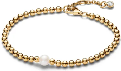 A close-up shot of a gold bracelet with a pearl and small diamond accent.