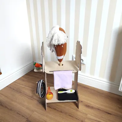 A toy hobby horse stall with accessories in a room with striped wallpaper.
