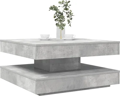 A square coffee table with a concrete-like finish, shown from a diagonal angle with two cups and a vase of greenery on top.