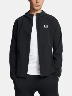 A man wearing a black Under Armour jacket and white t-shirt, standing against a light gray background.
