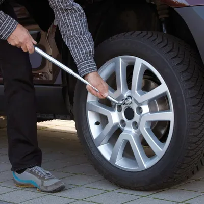 A person is changing a car tire using a lug wrench.