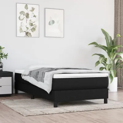 A bedroom scene with a mattress on a bed frame, two framed pictures on the wall, and a plant in a pot.