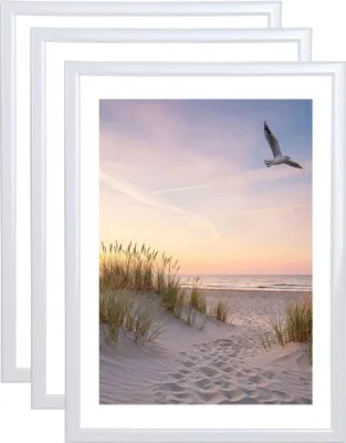 A stack of white picture frames with a beach scene inside the front frame.