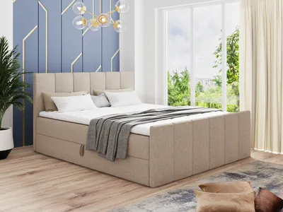 A bedroom scene featuring a beige upholstered boxspring bed with storage drawers, set against a blue geometric wall and a large window with a view of trees.