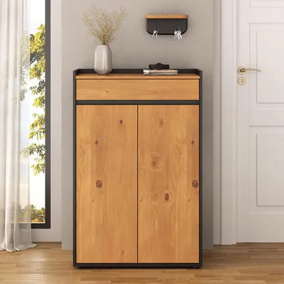 A shoe cabinet with two doors and a drawer, placed in a hallway next to a window and a door.
