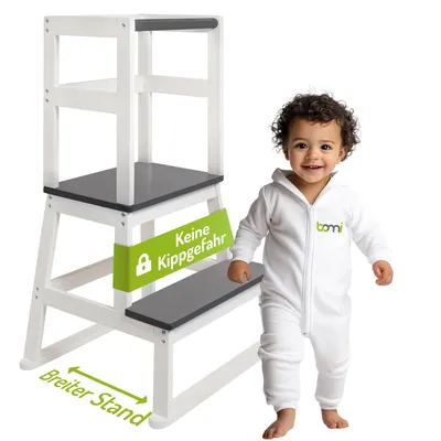 A child stands next to a wooden learning tower.