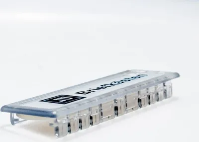 A close-up shot of a clear name tag with black text and a logo on a white background.