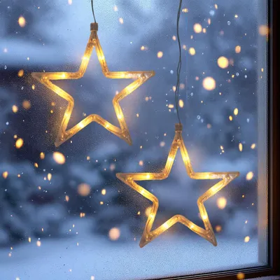 Two star-shaped LED lights hanging on a window with a snowy, blurred background.
