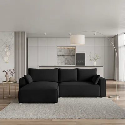 A modern living room with a black sectional sofa, a floor lamp, and a kitchen area in the background.