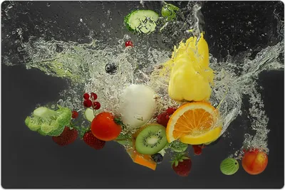 Various fruits and vegetables splashing into water against a dark background.