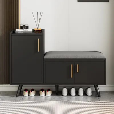 A black shoe cabinet with a gray upholstered bench top, featuring gold handles and a set of shoes underneath.