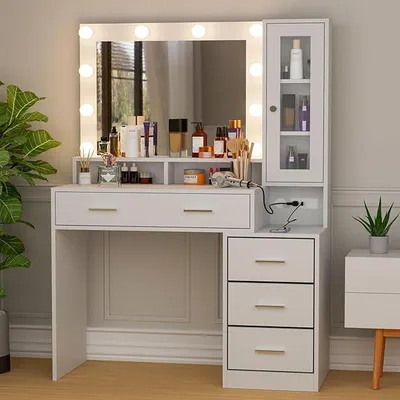 A white vanity table with a large illuminated mirror, drawers, and a side cabinet filled with cosmetics and toiletries.