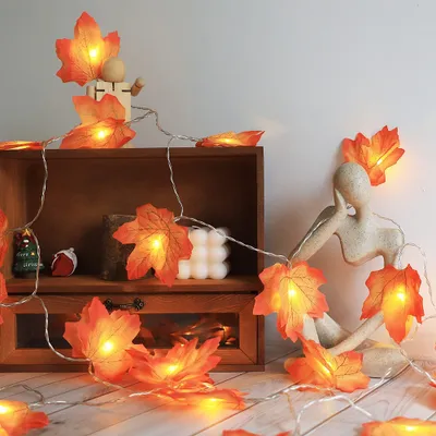 A string of LED lights shaped like maple leaves is draped around a wooden shelf and a decorative sculpture.