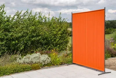 An orange privacy screen stands in a garden setting with plants and a paved patio.