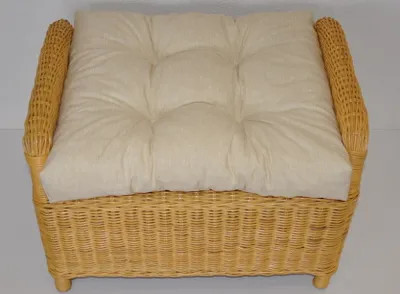 A close-up, front-facing view of a beige wicker ottoman with a tufted cushion.