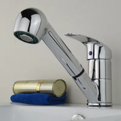 A chrome kitchen faucet with a pull-out spray head is shown on a white sink. A blue towel and a gold cosmetic bottle are placed on the sink next to the faucet.