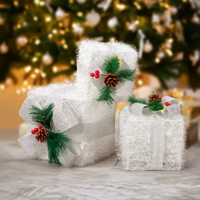 Illuminated Christmas gift boxes with pine cones and pine needles in front of a blurred Christmas tree.