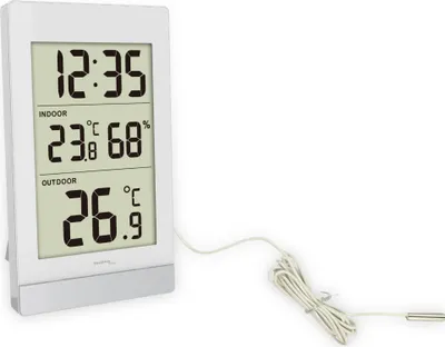 A digital weather station with a white frame and a light-colored screen displaying time, indoor temperature and humidity, and outdoor temperature. A white wire extends from the device to a small probe.