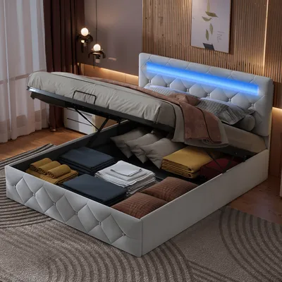 A bed with its storage compartment open, revealing neatly folded linens and pillows. The bed has a tufted headboard with blue LED lighting.