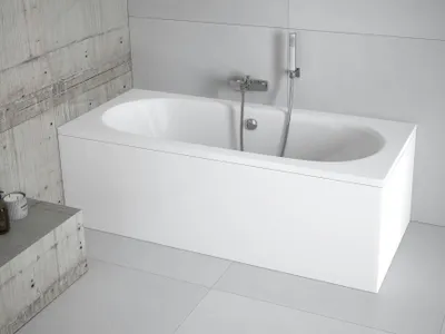 A white bathtub with a chrome faucet and shower head is shown in a modern bathroom with concrete and tiled walls.
