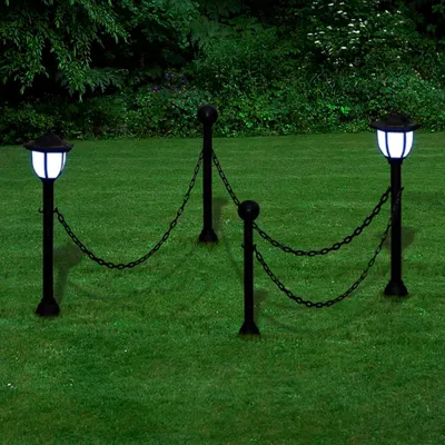 Two solar-powered garden lamps connected by a chain fence, set in a grassy garden with trees in the background.