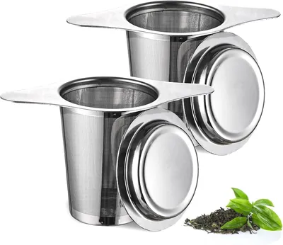 Two stainless steel tea infusers with lids and a small pile of loose leaf tea with a few green leaves.