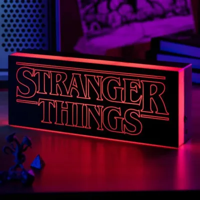 A Stranger Things logo light is displayed on a table, with some small figurines in the foreground.