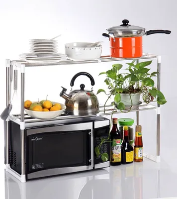 A kitchen shelf unit with a microwave, pots, bowls, fruit, and plants.