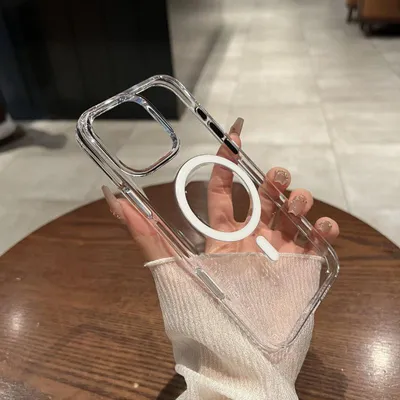 A hand holding a clear iPhone case with a white MagSafe ring on a wooden table.