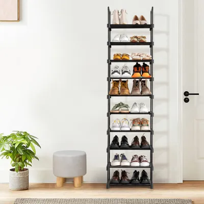 A tall, black, 10-tier shoe rack filled with various types of shoes, placed next to a gray upholstered stool and a potted plant in a neutral room.