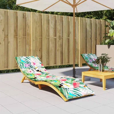 A patio scene with two chaise lounge chairs with tropical-themed cushions, a wooden table, and a large umbrella.